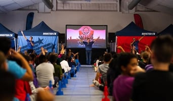 image of inside a school with students sitting on the floor and Booster celebrating