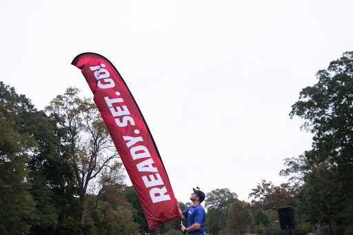 Booster team member with a blue shirt sets up a feather flag with the words 