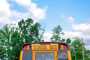 Back end of a yellow school bus, with a beautiful blue sky background.