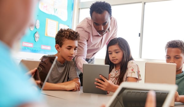 A teacher and two students working on a tablet at school