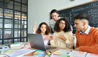 image of adults in a classroom talking in front of a laptop