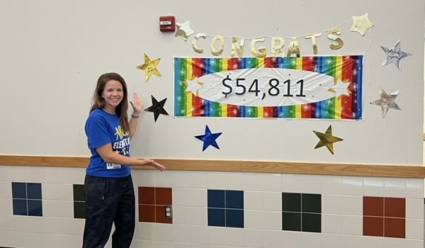 Image of April a PTA member presenting how much money they raised on a school wall