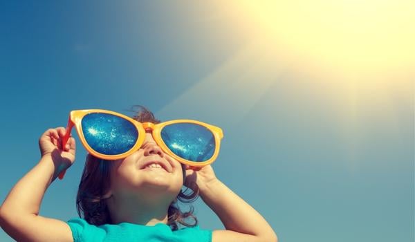 Little kid wearing big sunglasses looking up at the sun.