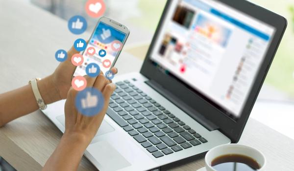 Image of laptop and a ladies hands in front  with her cellphone. 