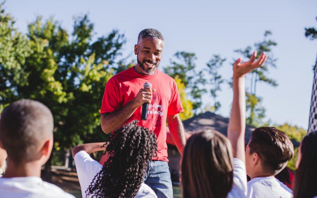 Man outside holding a microphone and talking to kids